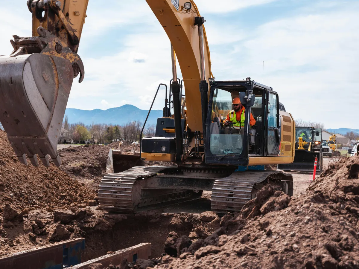 Tracked excavator with a raised boom and bucket beside an earthwork area.