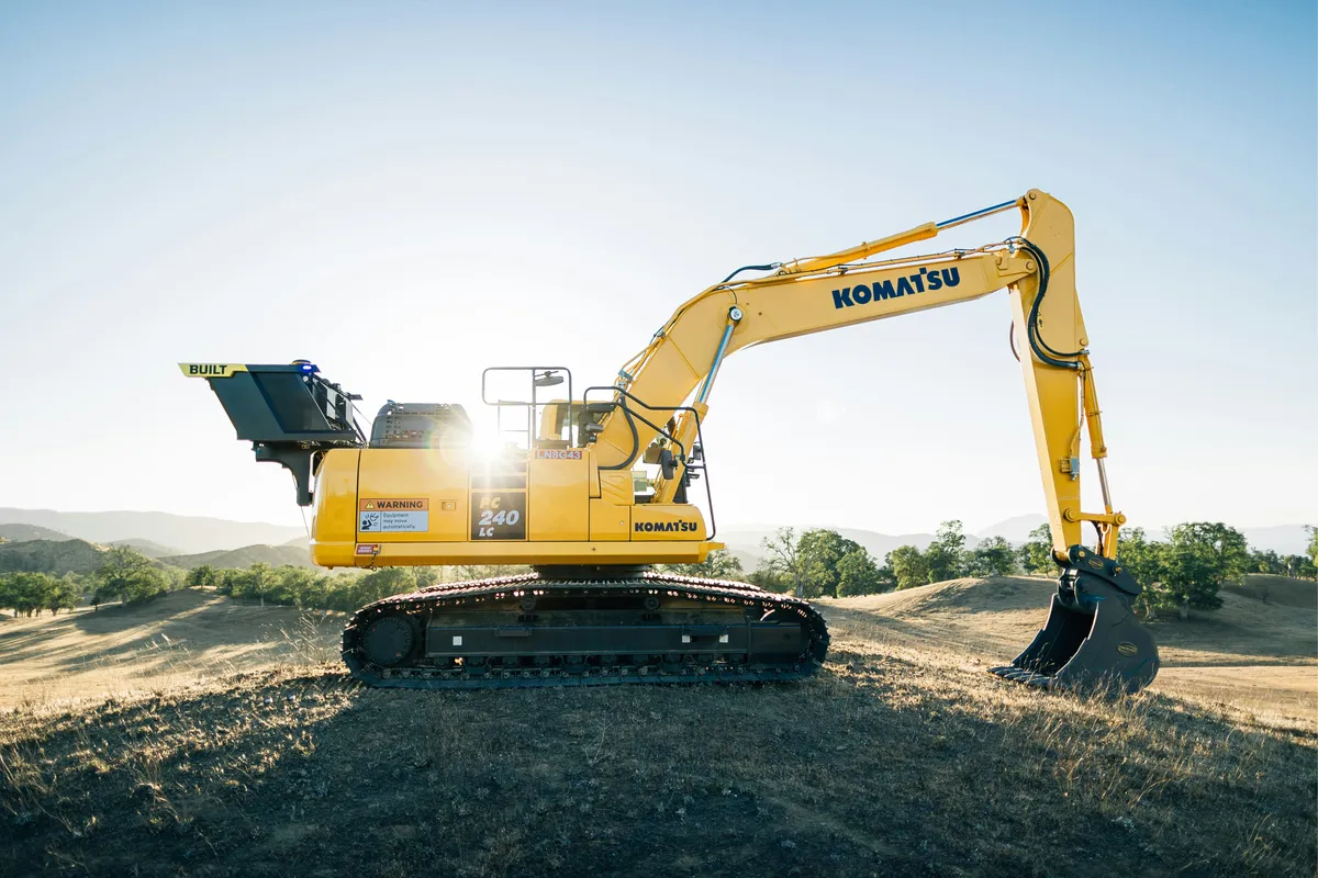 Yellow tracked excavator with its bucket extended beside an earthwork area.