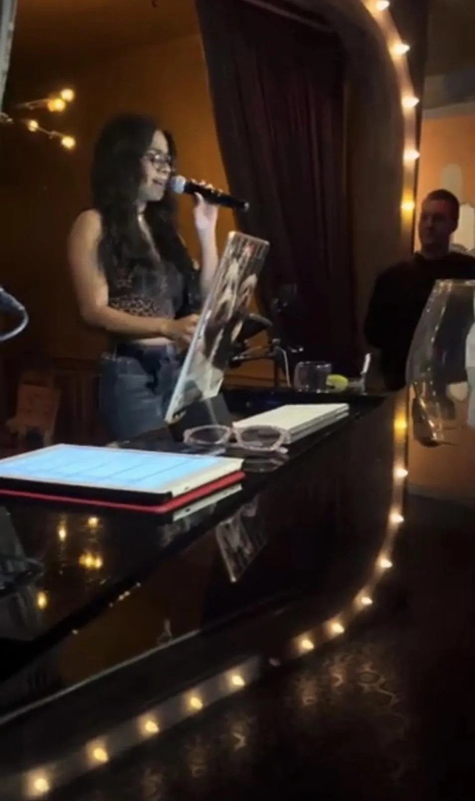Close-up black and white photo of a professional recording microphone with a sound screen in a studio setting.