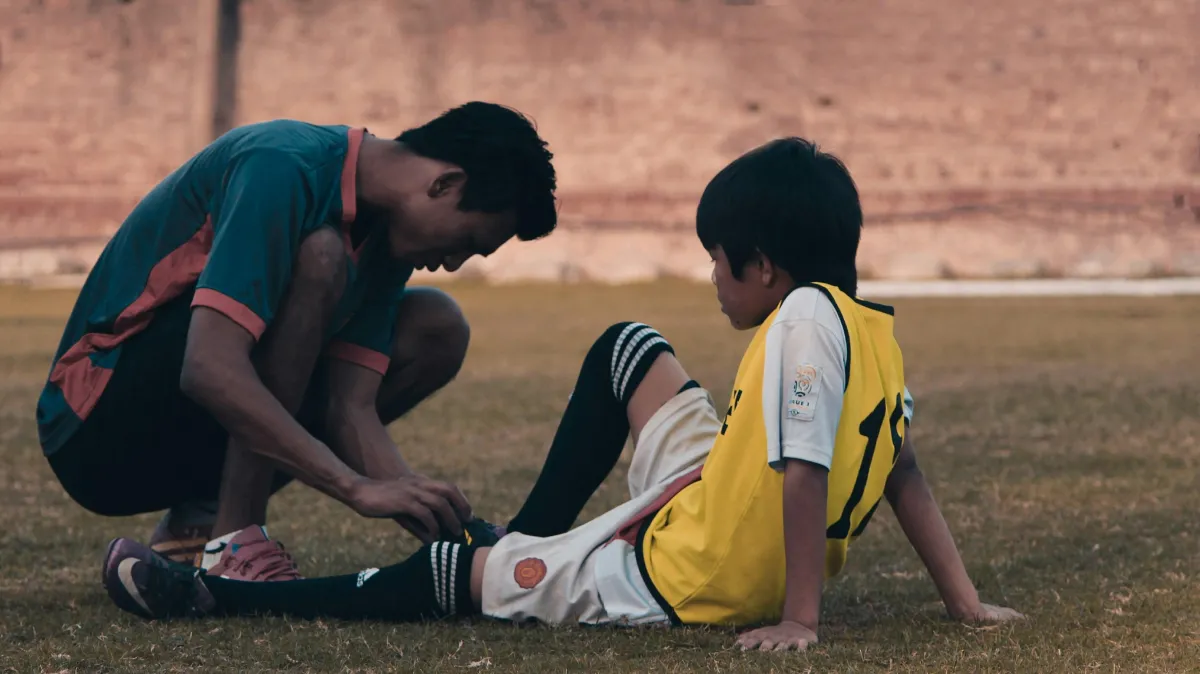 Child checking a teammate's hurt ankle on the soccer field after a possible sprain or strain