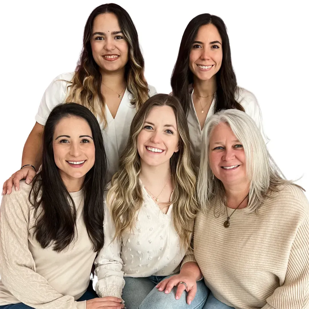 A smiling group of our five female doctors, posing together in a supportive group, all wearing white and neutral-colored tops.