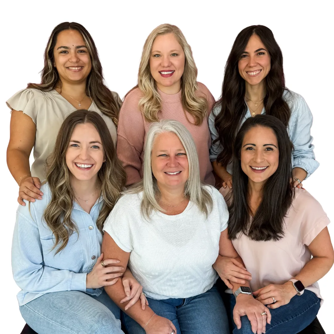 A smiling group of our five female doctors, posing together in a supportive group, all wearing white and neutral-colored tops.