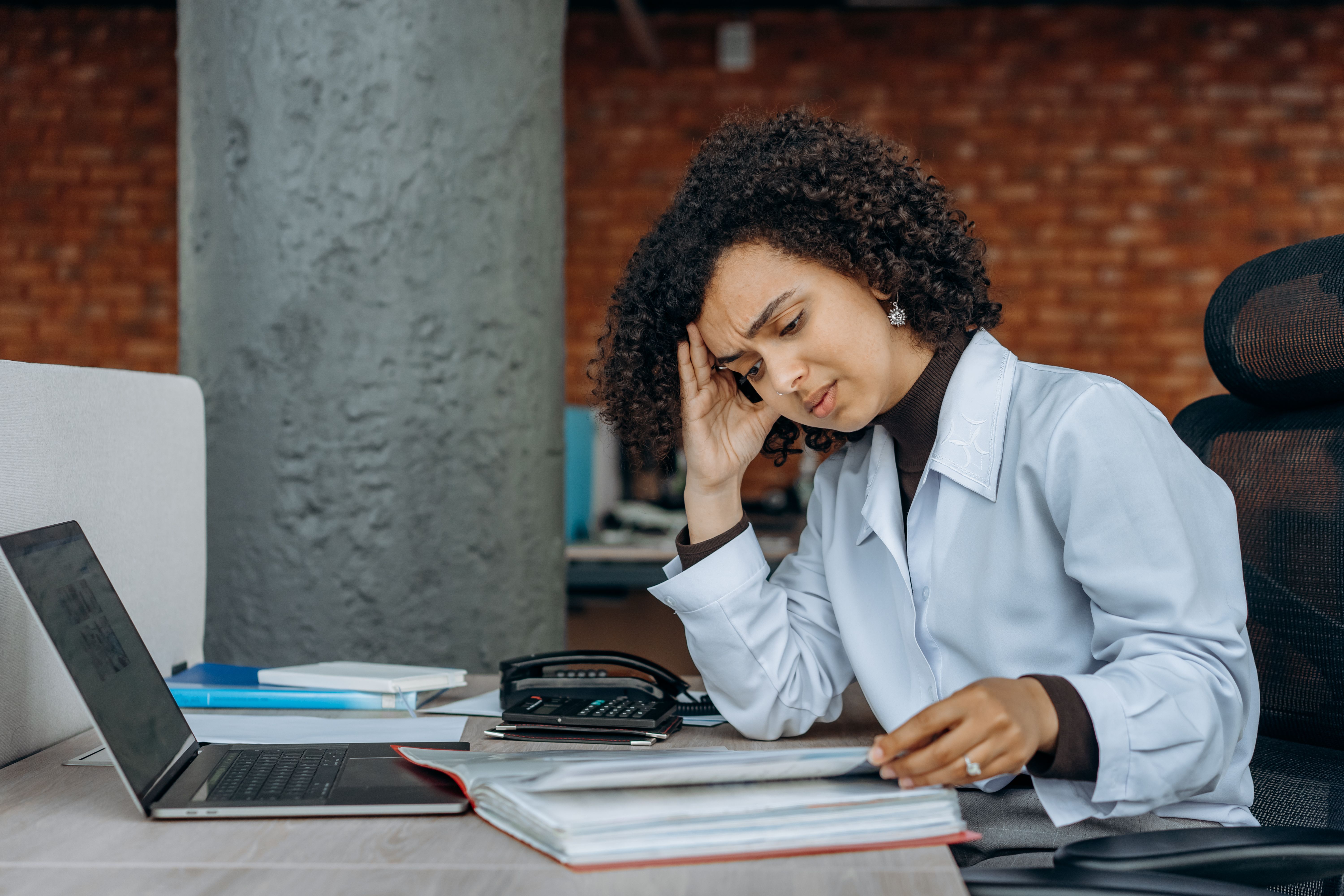 Stressed businesswoman rubbing her temple while reviewing paperwork at her desk