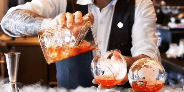 Bartender pouring a cocktail into glasses.