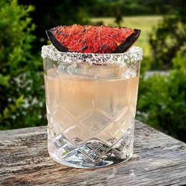 Cocktail in a glass with a salted rim and fruit garnish.
