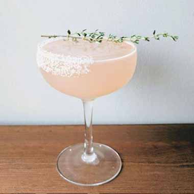 Cocktail in a coupe glass with a herb garnish.