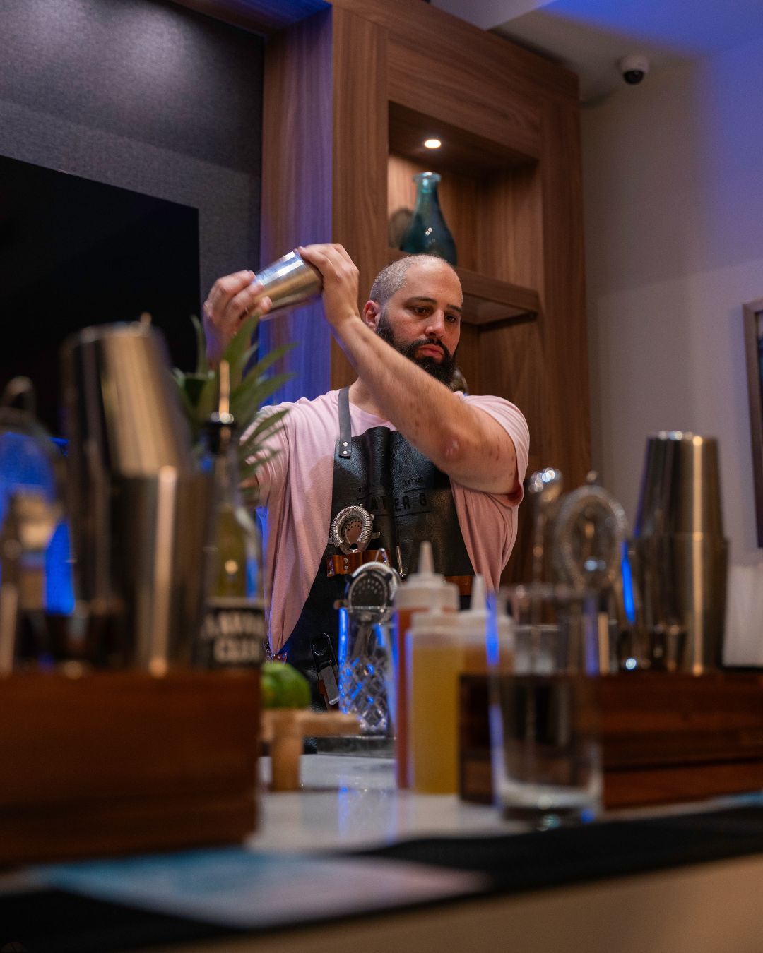 Bartender pouring a cocktail into a glass behind a bar.