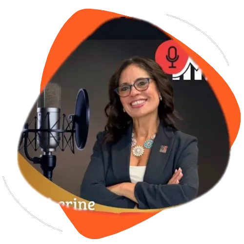 Katherine Martín-Fisher standing in front of a microphone wearing dark grey blazer and white shirt.