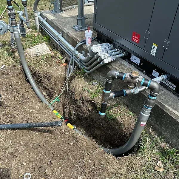 Professional plumbers from Beemer Plumbing are performing a new residential gas line installation at a home in Spring Hill, KS. A technician in a branded shirt is using a specialized tool to fuse sections of yellow polyethylene gas pipe within an excavated trench in the front yard. A second technician manages a coil of the pipe, while a company service truck is visible in the driveway of the high-end suburban property, showcasing the expert Gas Line Installation & Repair services provided by Beemer Plumbing.