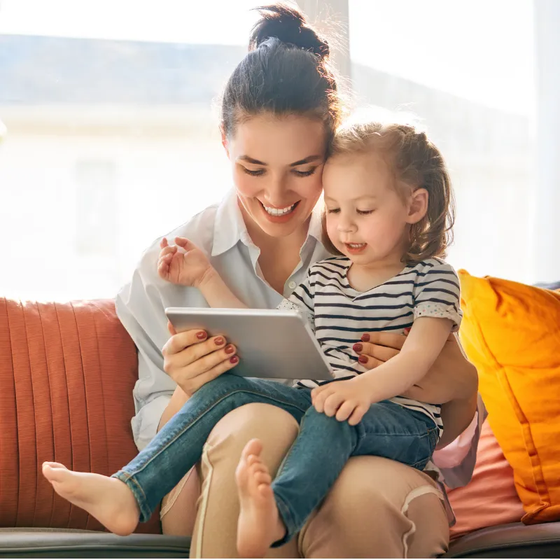Smiling mom with toddler on her lap watching iPad together, illustrating bonding, learning, and nurturing joy for busy moms by watching my YouTube channel: Moms Simply Thriving