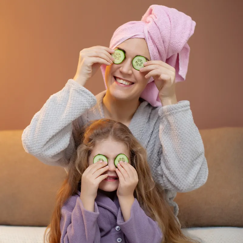 Mom and daughter in robes with cucumber slices over eyes, showing playful connection and relaxation while learning home study courses