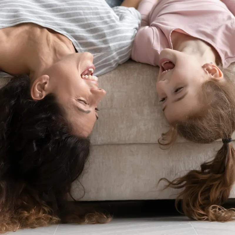 Mom and daughter lying upside down on a couch, laughing and connecting with ease, representing joyful mother-child moments