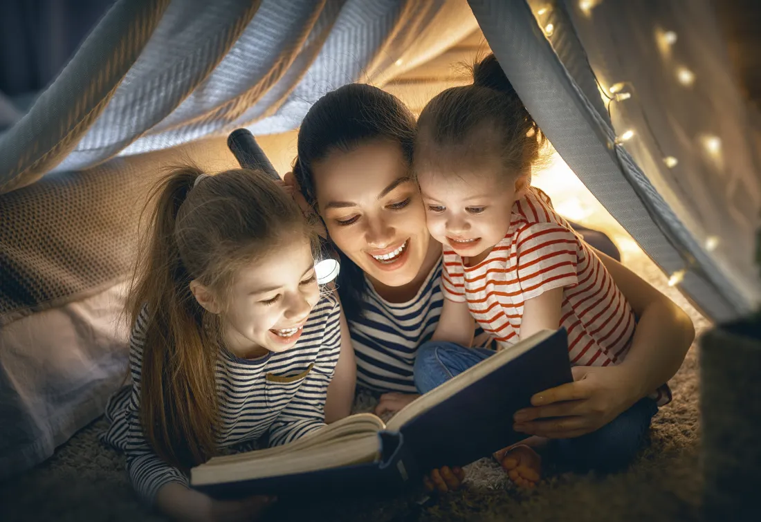 Mom reading under a cozy blanket fort with her two kids, enjoying playful, present moments that reflect thriving with ease for overwhelmed moms