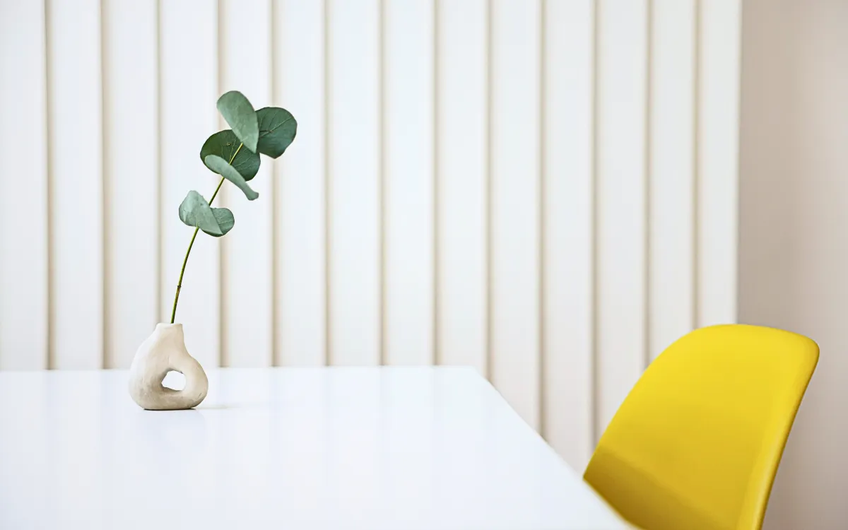 Bright white table with yellow chair and green decorative plant, representing a calm and nourishing space for overwhelmed moms seeking ease and focus