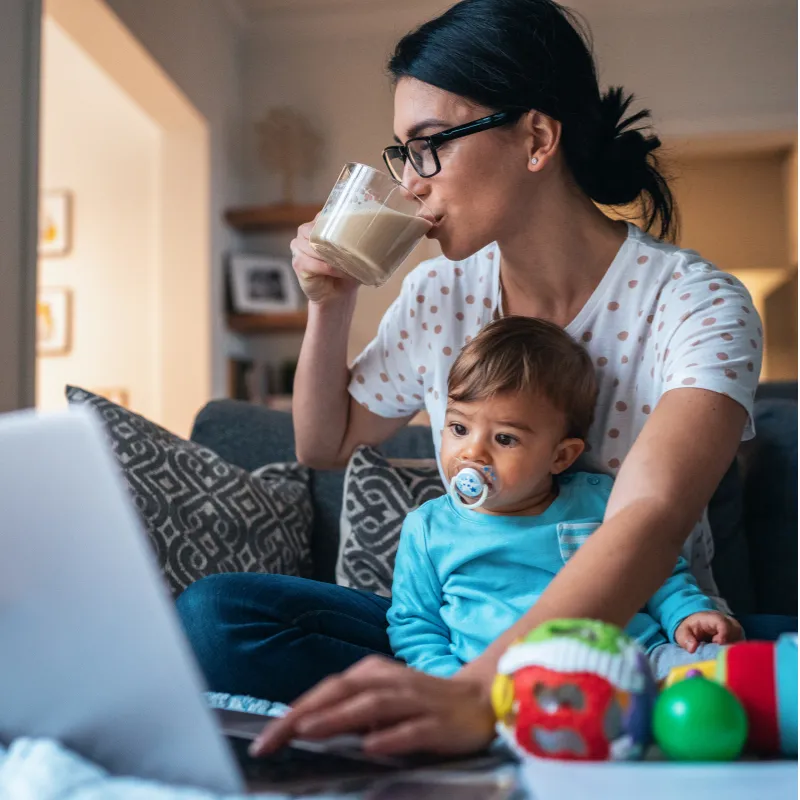 Busy mom multitasking with baby, laptop, and cappuccino, illustrating accessing trusted online resources and support for motherhood