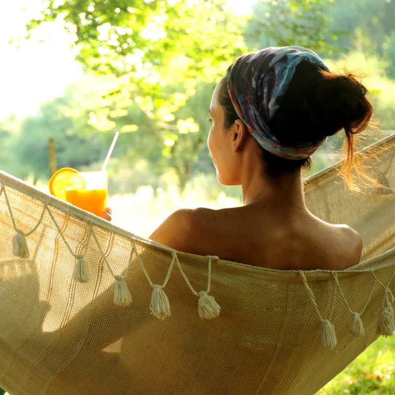 Relaxed mom in hammock holding fresh smoothie, illustrating calm, restorative energy, and effortless lifestyle