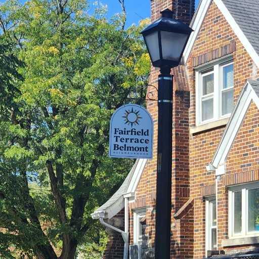 A multi story red brick home with a  large tree in the front yard, and centered in the image a phone pole with a Fairfield Terrace Belmont Neighborhood sign attached at the top.