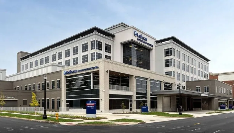A large white multistory building with black windows on a street corner with a sign in blue that says "Lutheran Downtown Hospital"