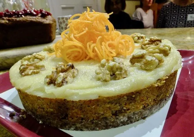 Raw carrot cake piled with macadamia cream cheese frosting, walnut halves and fine carrot ribbons piled on top