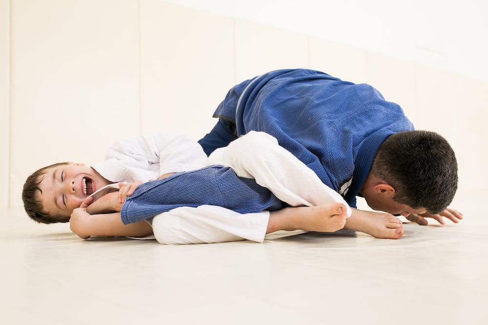 Child practicing Brazilian Jiu-Jitsu with an adult partner