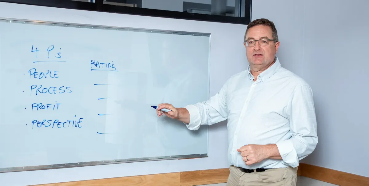 Paul standing at a whiteboard during a 4P Flight Plan workshop, sketching process improvements for a growing team.