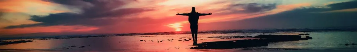 Photo of man with arms outstretched, silhouetted against the sunset, at the beach