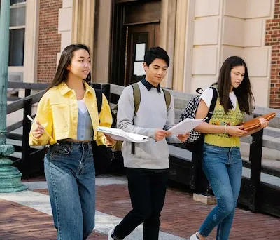 Three university students walking across campus carrying folders