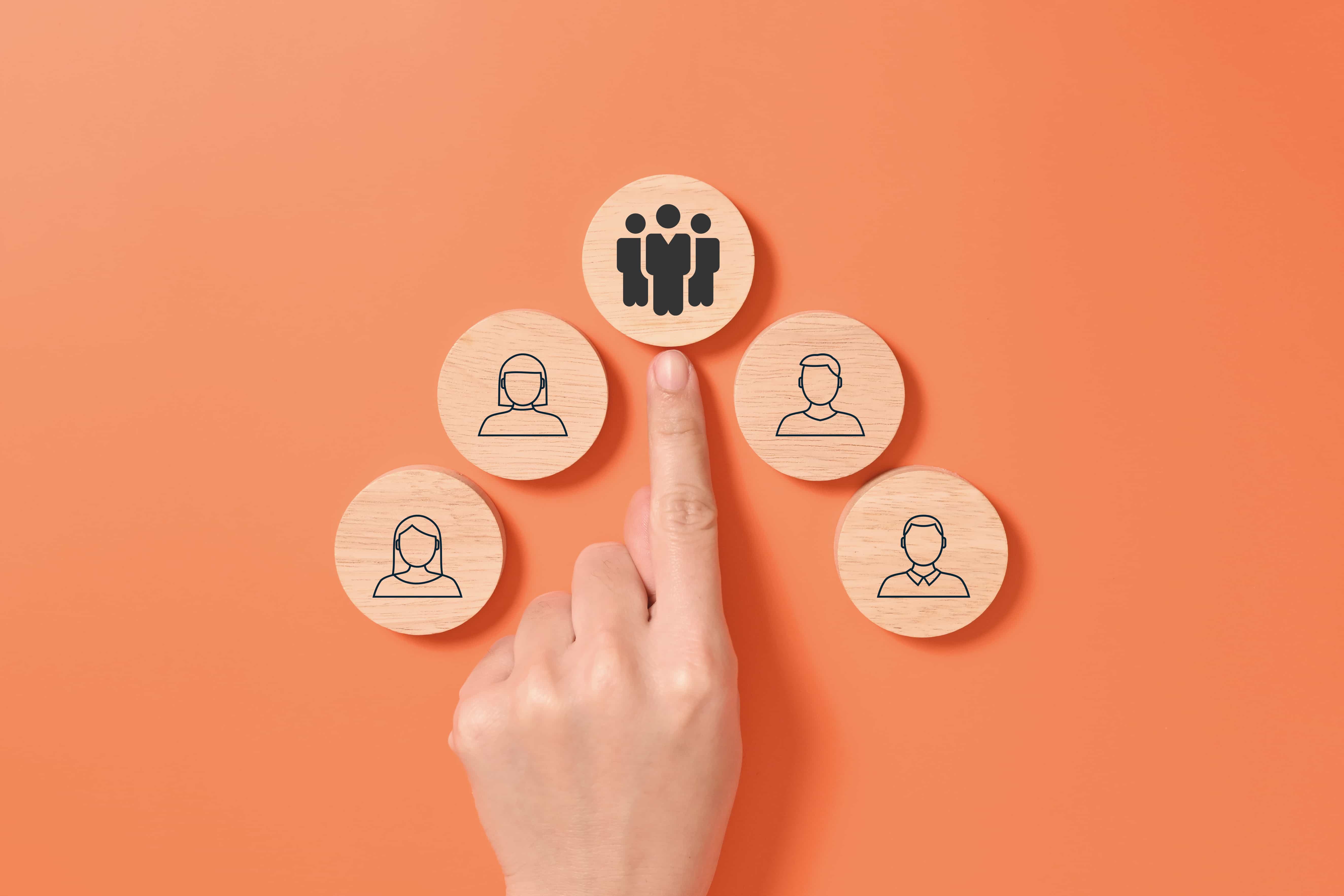 A hand pointing to a wooden block representing leadership above a team of employees, symbolizing strategic team management service in Chicago, IL.