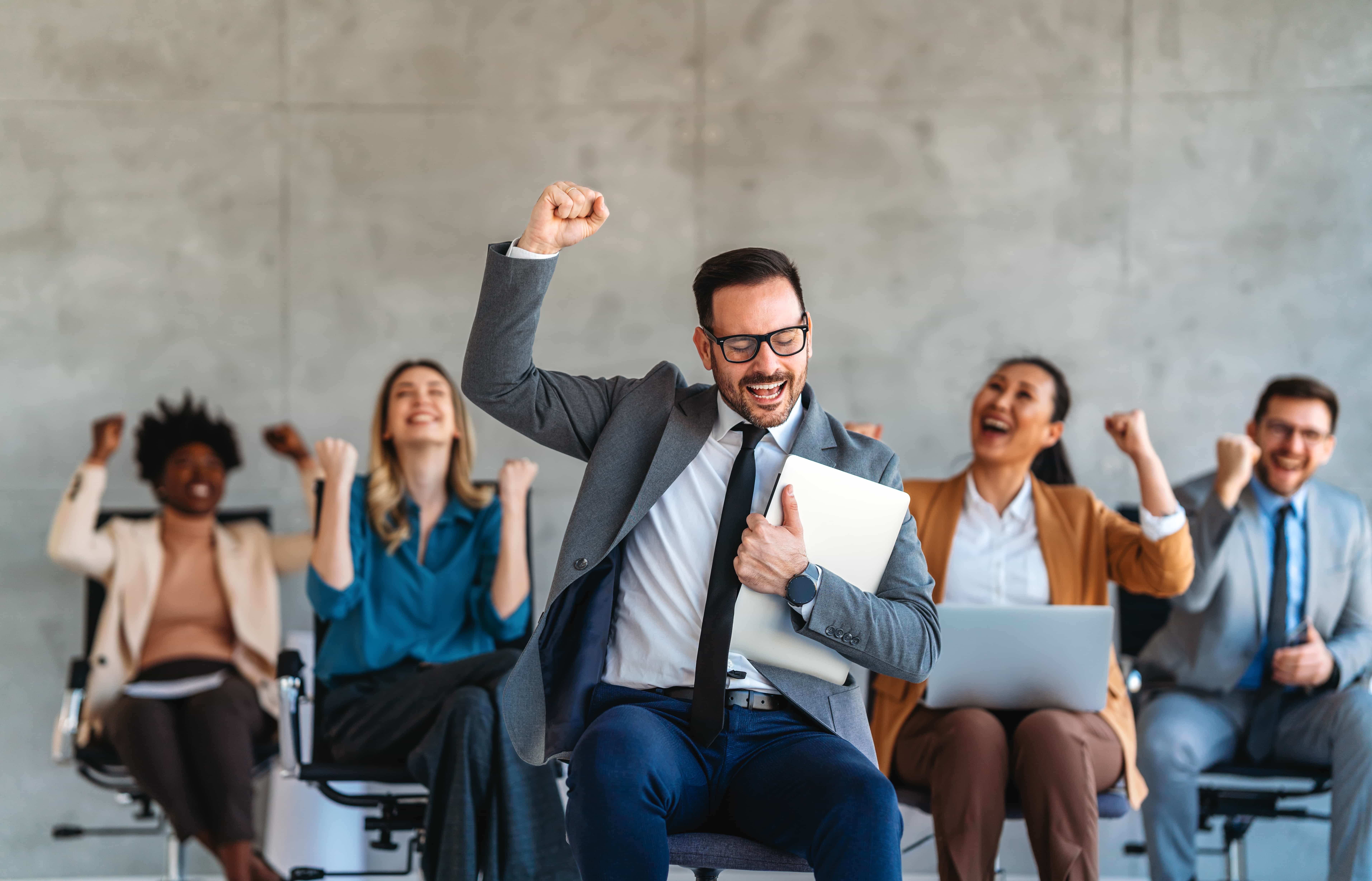 A cheering team of diverse professionals celebrating a major milestone during a Sales Performance Coaching session in Florida.