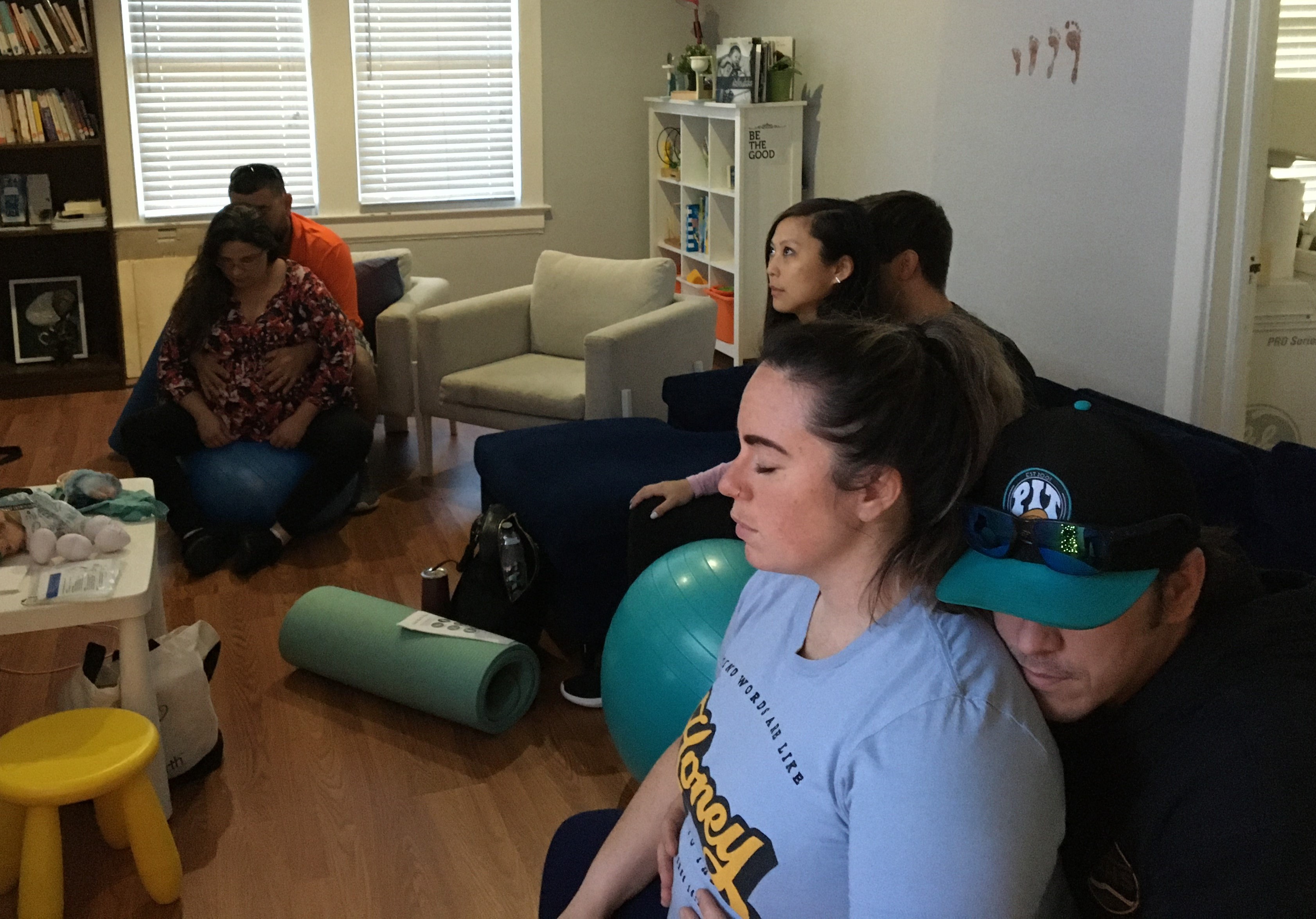A young family of three, including a newborn, sitting together on a cozy living room sofa. The parents are smiling at their baby, radiating joy and gratitude. The room is softly lit, with gentle colors and a relaxed, homey atmosphere.