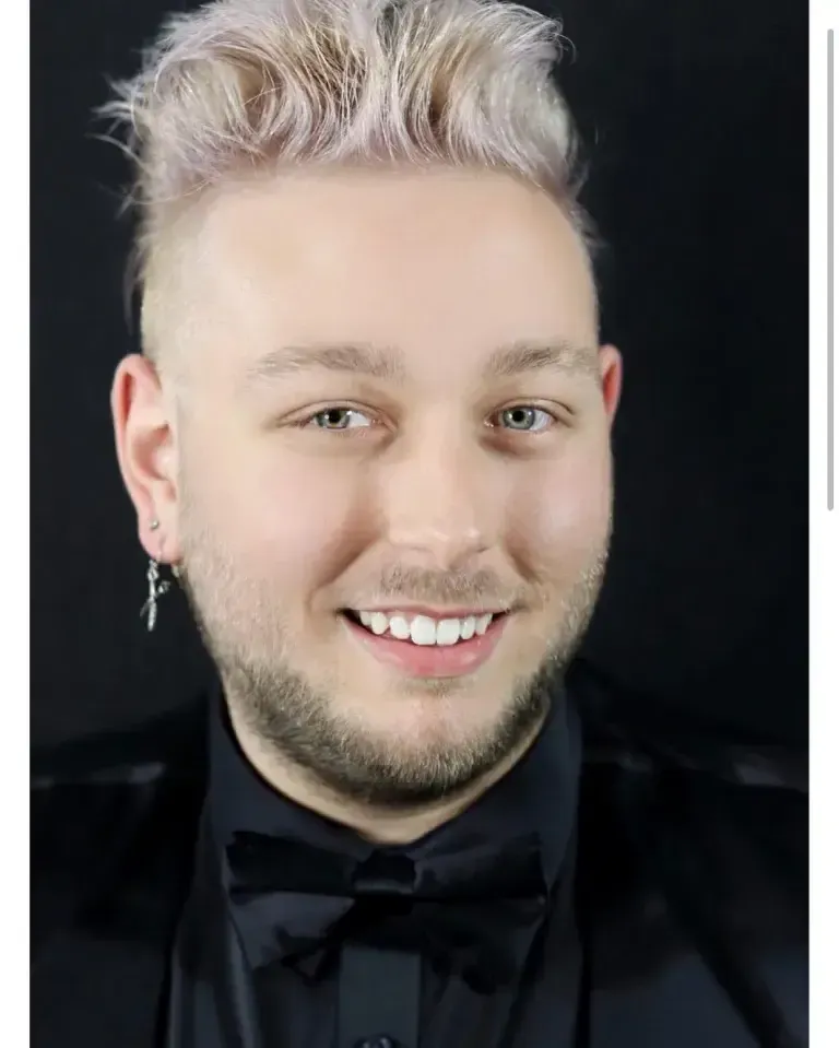 Head shot of salon owner and stylist rob brown with blonde hair wearing black and a scissor earring 