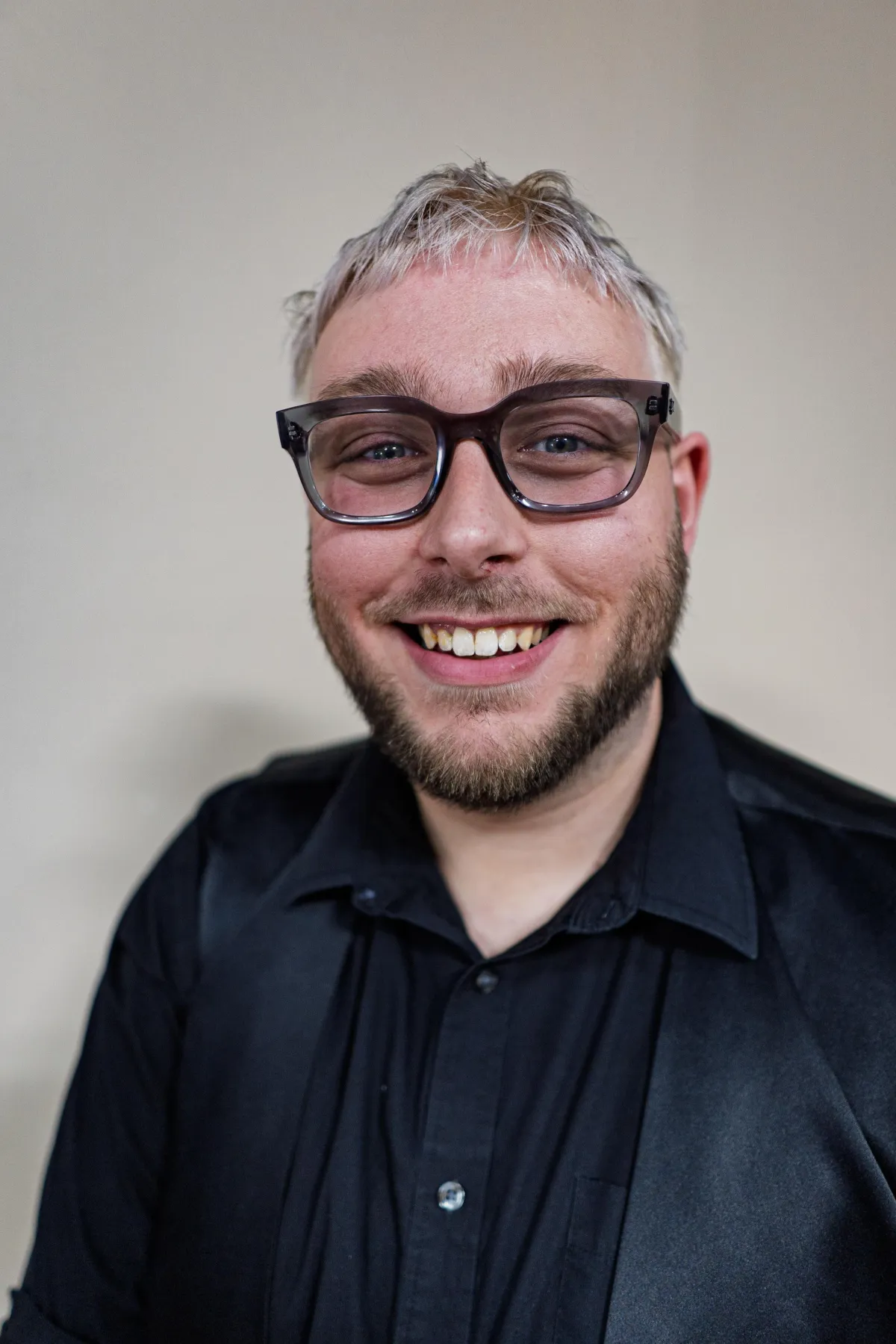 Head shot of salon owner and stylist rob brown with blonde hair wearing black and a scissor earring 