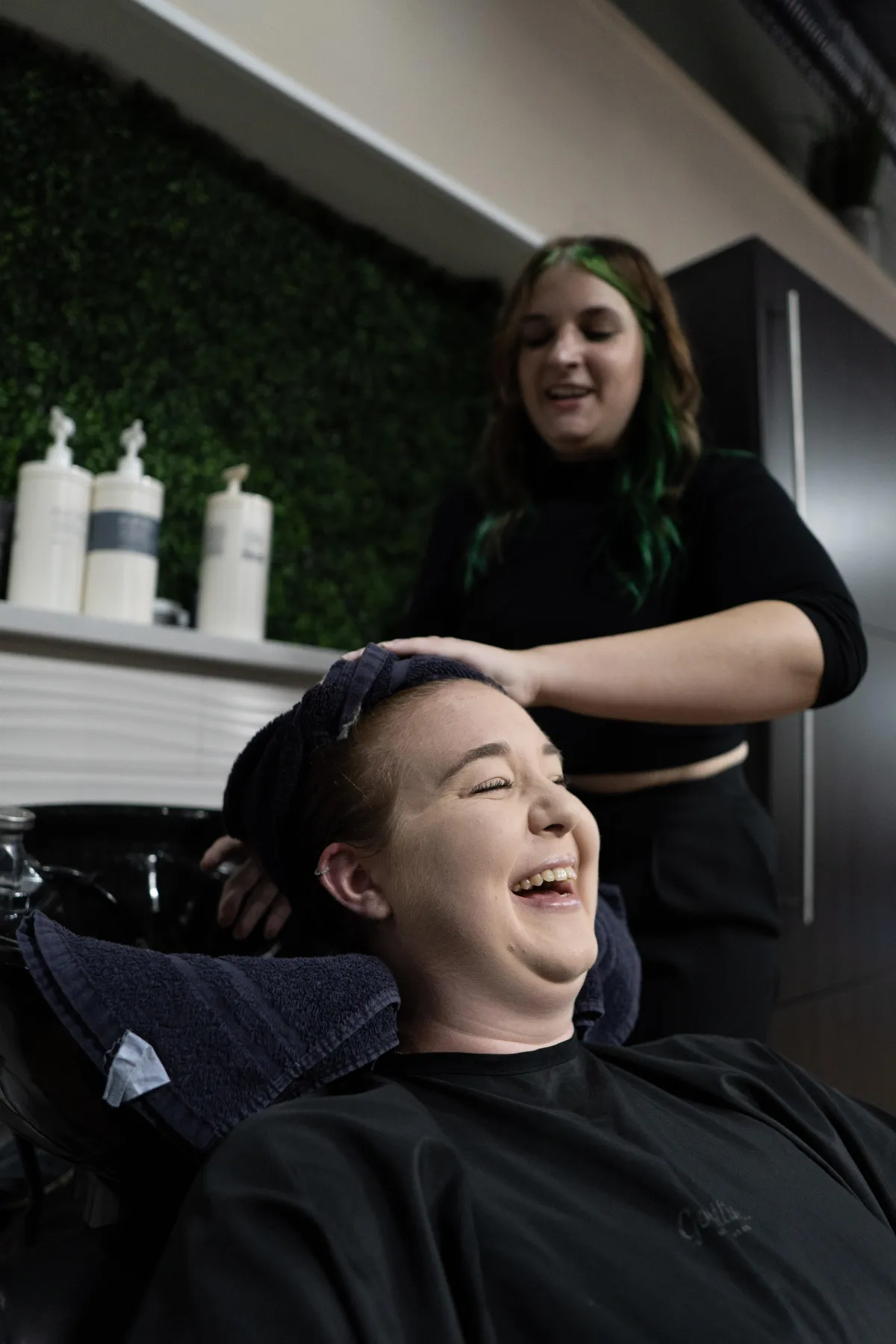 Emily Keoppen shampooing her client at the shampoo bowl in avera hair studio. Emily is wearing black cloths with and they are both smiling using eufora international haircare.