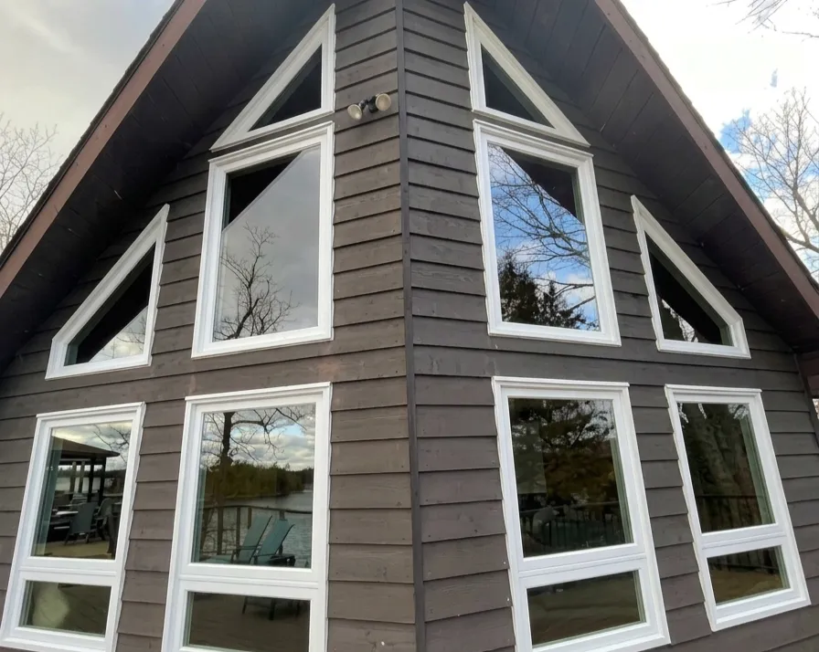 Custom white geometric windows on a dark brown A-frame cabin with waterfront reflections