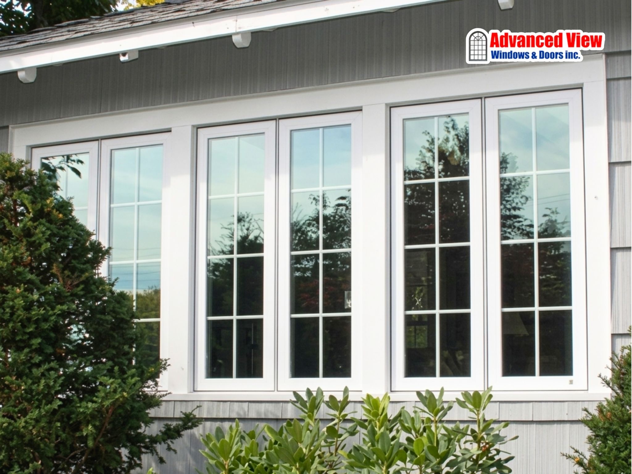Modern white multi-panel windows with a grid pattern on a home with grey siding and outdoor landscaping.