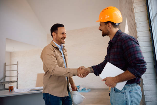 Contractor and client shaking hands at a construction site, finalizing a home renovation project.