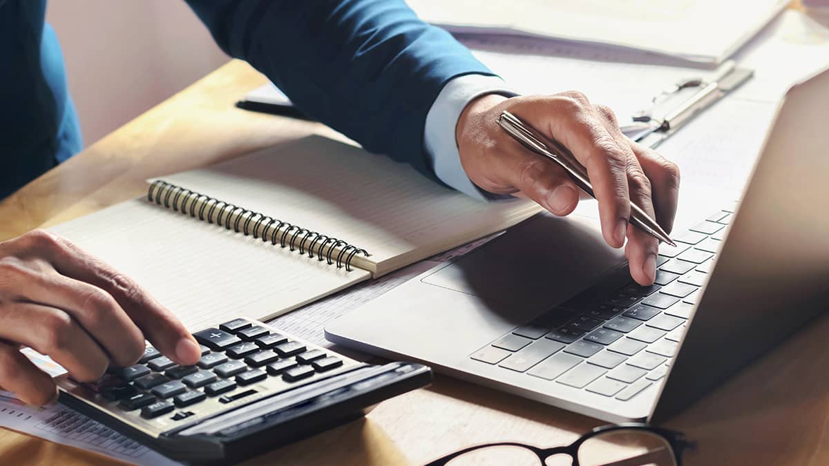 Accountant using a calculator and laptop to complete financial reports and payroll calculations.