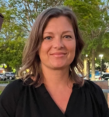 Professional woman smiling outdoors in a park setting with trees and natural evening light.