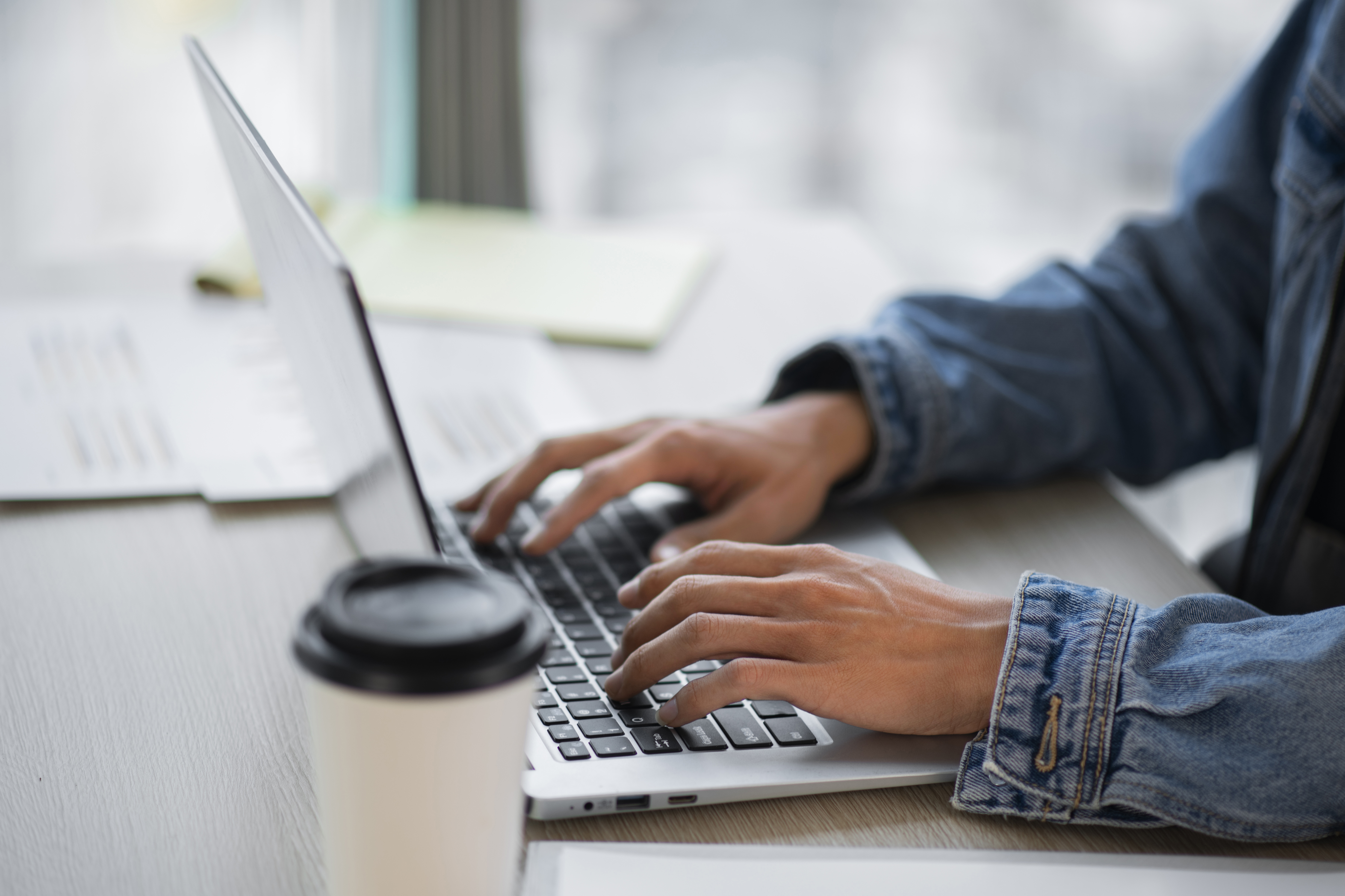 Person working on a laptop at a desk with documents and coffee cup — bookkeeping and accounting work for JG Financial Services.