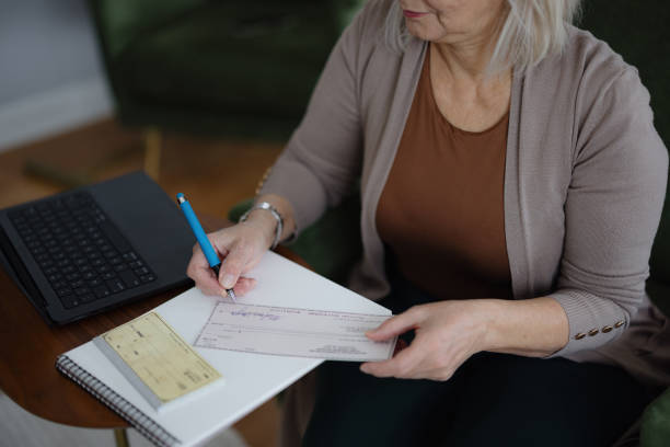 Senior woman filling out a check while managing finances at home for payroll processing.