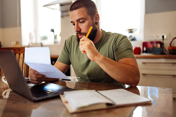 Man reviewing tax documents and financial papers while preparing his taxes on a laptop at home