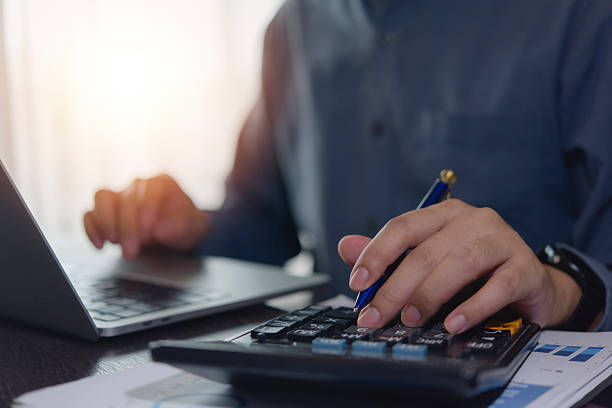 Business professional reviewing payroll data with a calculator and laptop during financial reconciliation.