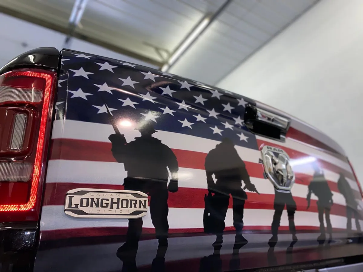 " Professional Car Wrap Installation service on a Dodge Ram Back Tailgate Door with image of the American Flag and Silhouette of Veterans by GB Enterprises AutoCare, located in Green Bay, WI . High-quality application on vehicle, demonstrating expert craftsmanship and attention to detail."