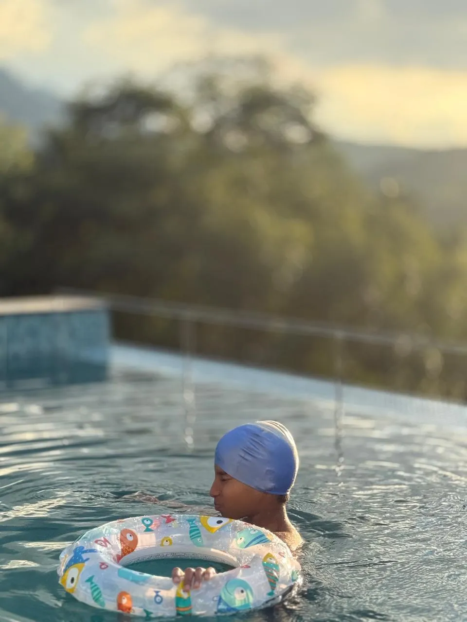 A peaceful garden path lined with flowering shrubs, leading to a cozy reading nook under a large banyan tree. The setting is tranquil, with dappled sunlight and birds visible in the background.