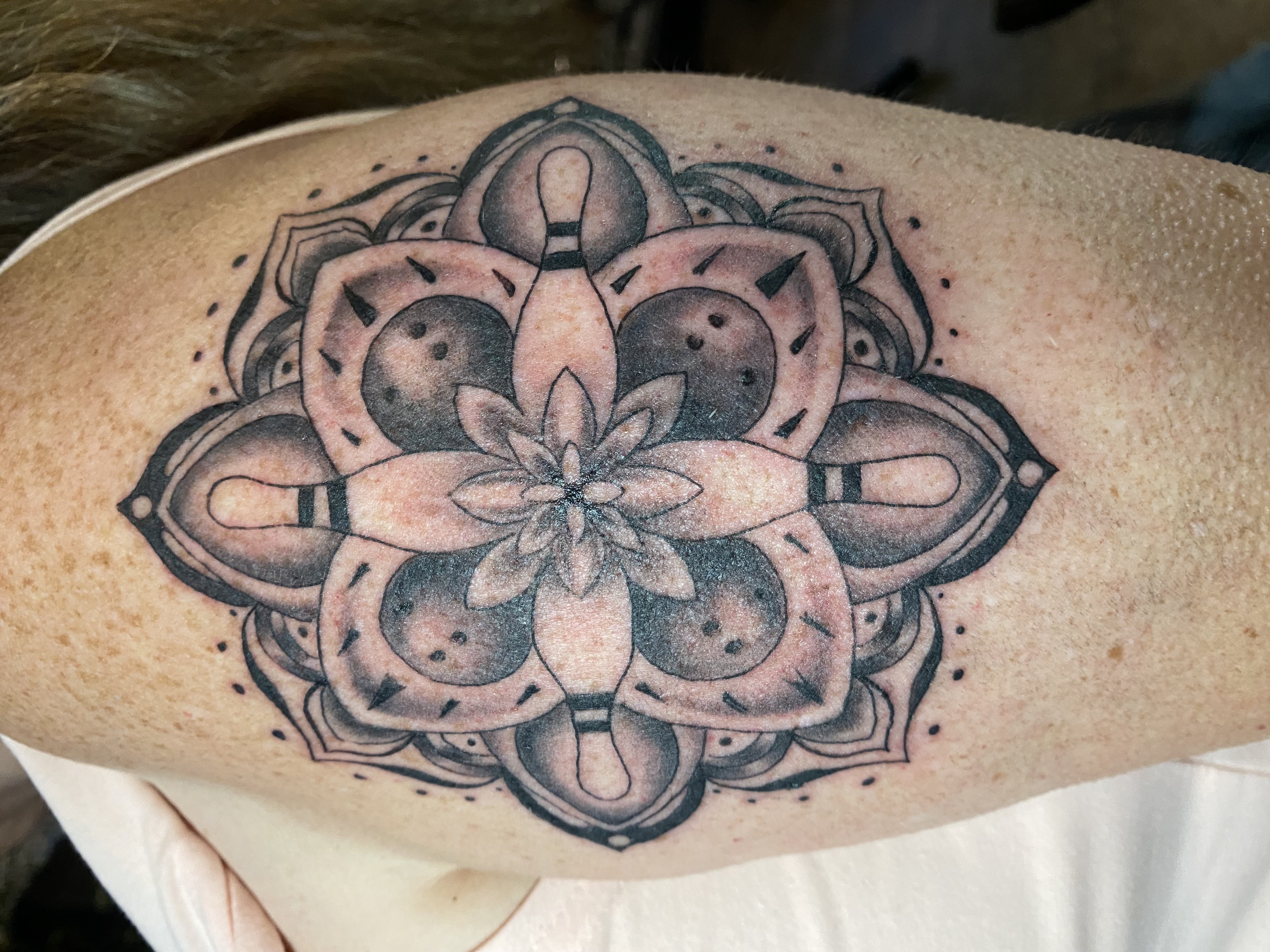 Close-up of a forearm tattoo featuring intricate geometric patterns in black ink, photographed in soft natural light. The background is a blurred studio setting with warm neutral tones. 1:1 aspect ratio.