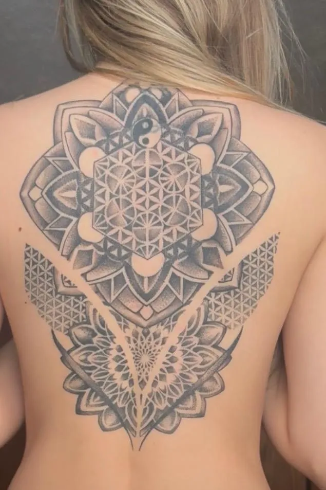 Close-up of a forearm tattoo featuring intricate geometric patterns in black ink, photographed in soft natural light. The background is a blurred studio setting with warm neutral tones. 1:1 aspect ratio.