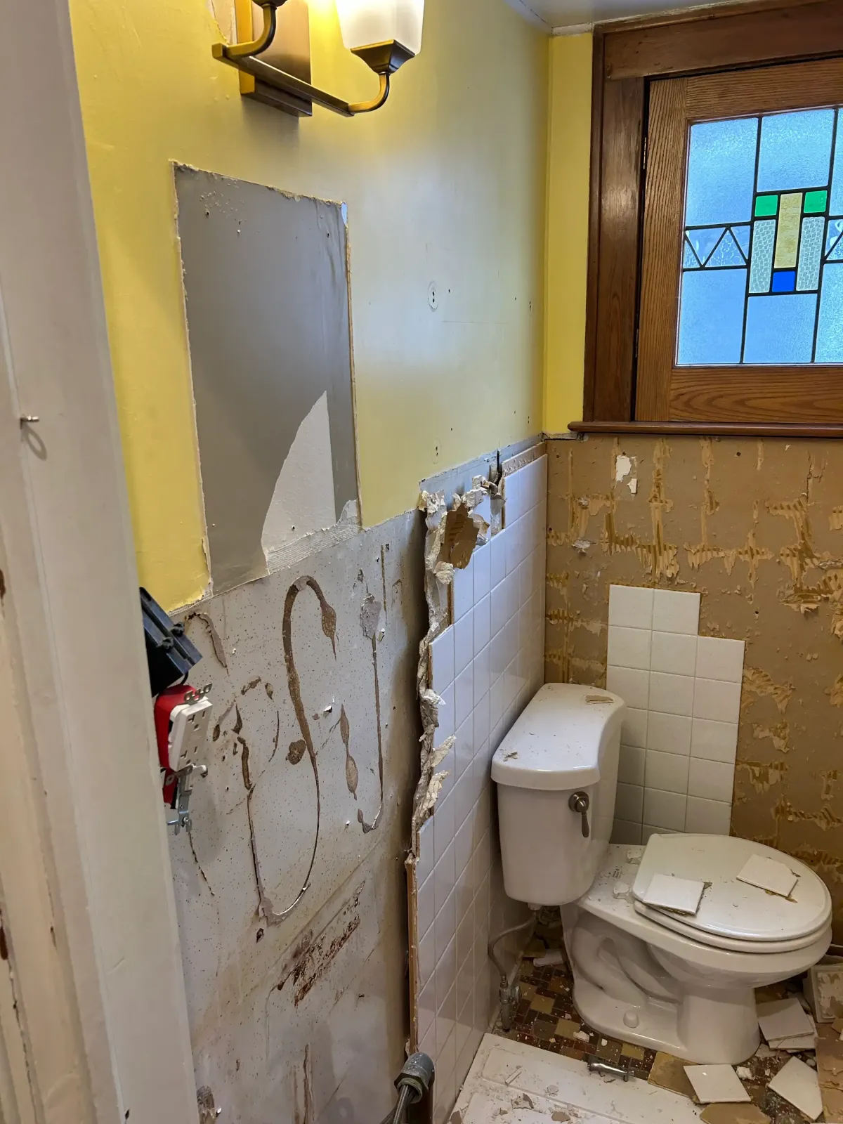 Bathroom demolition in a historic West Michigan home featuring a preserved stained glass window and careful removal of lath and plaster walls by Archstone Homes.