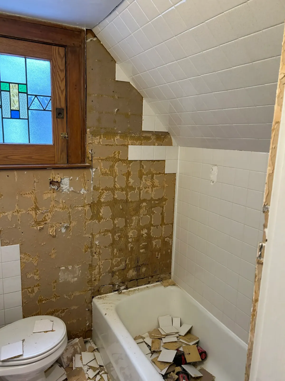 Contractors removing old bathroom tile and mud set to expose the original wall substrate for a custom tile renovation in West Michigan.