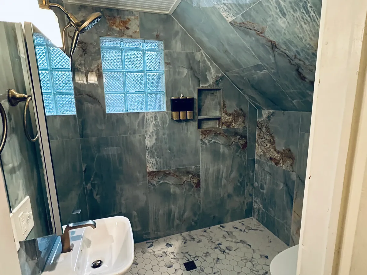 Contractors removing old bathroom tile and mud set to expose the original wall substrate for a custom tile renovation in West Michigan.