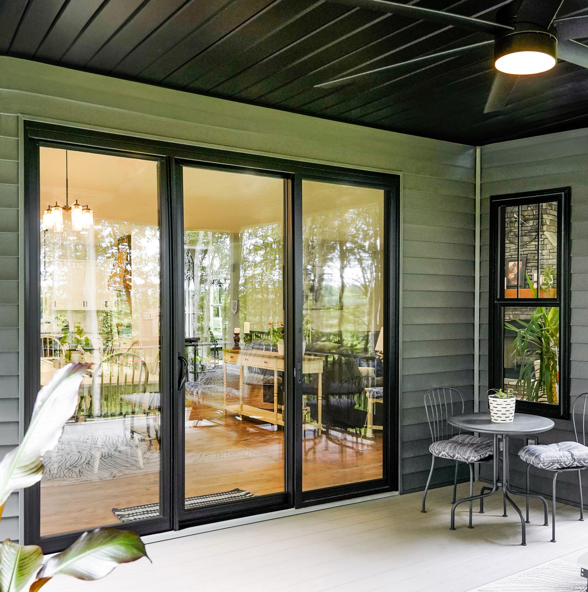 A modern living room with large, custom high-efficiency windows and a sleek glass door, sunlight streaming in, lush greenery visible outside, contemporary furniture, and a cozy, inviting atmosphere.